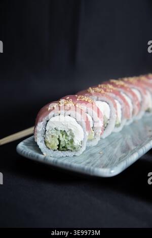 Fresh Tuna Sushi Roll with Cream Cheese, Avocado and Cucumber topped with Sesame Seeds on a Grey Ceramic Plate, Japanese Cuisine, Dark Mood Background Stock Photo