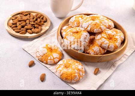 Almond crinkle cookies, dusted with powdered sugar, arranged in a simple wooden bowl and on a linen napkin, with raw almonds scattered nearby, offerin Stock Photo
