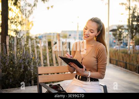 Woman creating digital art using stylus on tablet outdoors Stock Photo