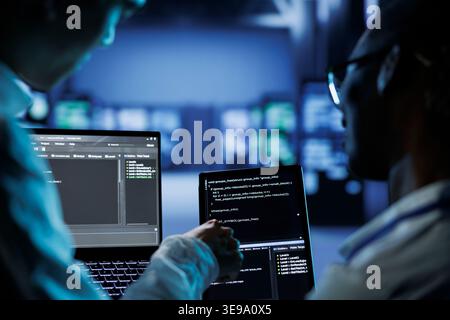 Teamworking colleagues building firewall systems in server room housing advanced infrastructure. Coworkers running code on tablet and laptop to upgrade data center rigs handling demanding workloads Stock Photo