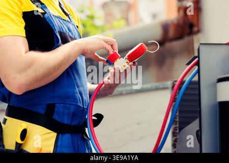 Experienced wireman doing annual air conditioner maintenance, assembling pressure measurement device before starting work. Licensed serviceman refilling cooling system refrigerant tank Stock Photo