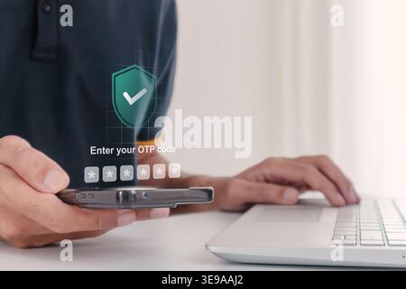A man using a laptop and smartphone to log in by entering One Time Password code. Two factor authentication OTP code for secure login. Stock Photo