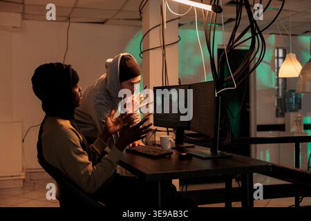 Team of online criminals hacking computer system at night, looking at firewall encryption before breaking into server. Planting virus to cause malware and access database, cyberterrorism. Stock Photo