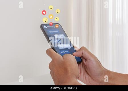 A man typing a message on his smartphone with social media emojis floating on the screen Stock Photo