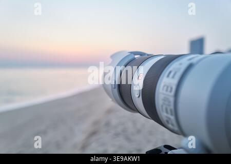 A blurred telephoto lens aims at a calm beach during a pastel-colored sunrise. The scene beautifully captures the passion for landscape photography. Stock Photo