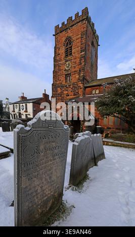 Frosted old gravestone in snow at St Wilfrid’s Churchyard, Grappenhall, with the historic red sandstone church tower. Stock Photo