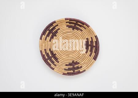 Handcrafted circular woven bowl featuring intricate geometric designs in dark purple and natural straw fibers, shown from a top-down perspective on a Stock Photo