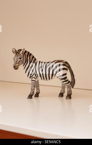 A realistic plastic zebra toy figurine featuring classic black and white stripes stands on a clean neutral surface against a minimalist background, pe Stock Photo