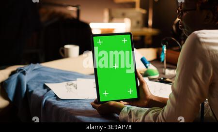 Designer using greenscreen on tablet, looking at modern chroma key display in atelier workshop. Couturier holding device with isolated mockup on screen, custom made tailoring. Close up. Stock Photo