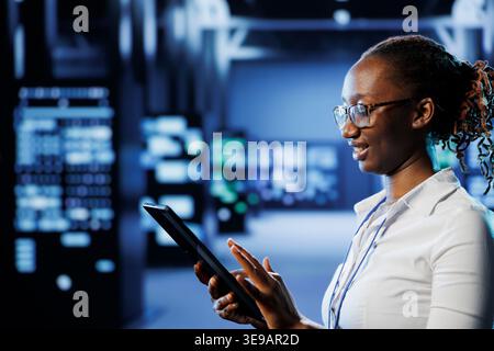 Carefree admin in high tech workspace uses tablet to prevent system overload. Meticulous expert between server units ensuring enough network bandwidth for smooth operations Stock Photo