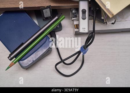 A white desk displays various storage devices, from stacked HDDs to a modern NVMe SSD. Cables and a green pencil complete this authentic IT workspace. Stock Photo