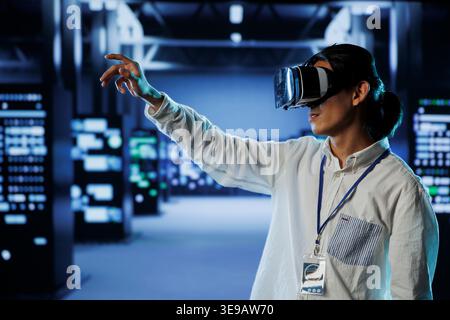 Licensed engineer in data center uses virtual reality to prevent system overload. Professional with VR goggles in server room ensuring enough network bandwidth for smooth operations Stock Photo