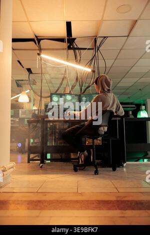 Asian IT specialist planting anonymous attack on government network, creating malware to access sensitive information on database. Young man using muliple monitors at night time. Stock Photo