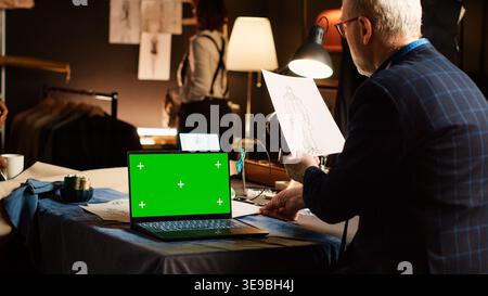 Fashion couturier with greenscreen reviewing sketches to create clothing line for modern items, handcraft concept. Senior designer working with isolated mockup display. Tripod shot. Stock Photo