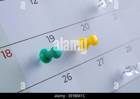 paper calendar with green and yellow push pins marking dates. Concept of scheduling, deadlines, reminders, organization and time management. Stock Photo