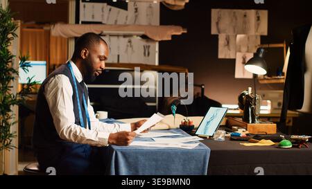 Craftsman checking sketches on laptop, working in atelier to create modern design. Couturier crafting new clothes collection in tailor workshop, small business concept. Tripod shot. Stock Photo