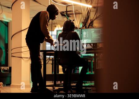 Online criminals analyzing script codes to hack government system, attacking sensitive sever and causing security breach. People hacking network and stealing information at night. Stock Photo