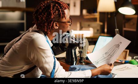 Designer using sewing machine to design custom made clothes, craftsmanship concept. Female couturier working on fashion collection in tailor workshop, handmade items clothing at table. Stock Photo