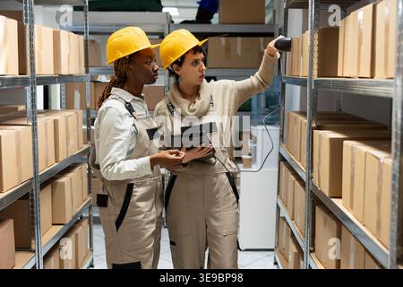 Group of diverse logistics workers handles registration and scanning goods. Team of women using scanner and tablet on pallets and packages, prepared for import export in warehouse. Stock Photo
