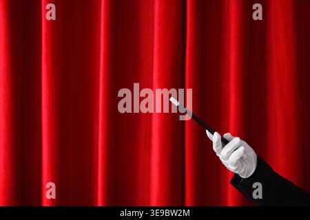 Magician's hand with wand near red curtain Stock Photo