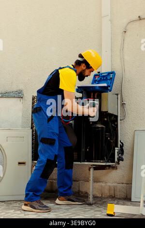 Licensed serviceman using electric drill to fix system issues caused by faulty expansion valve. Skilled expert working on damaged condenser requiring professional intervention Stock Photo