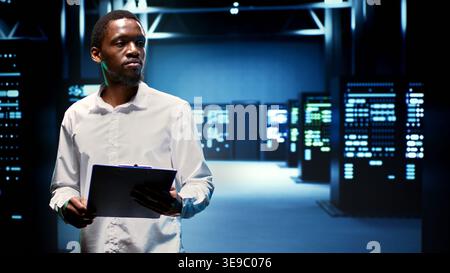 African american engineer in data center housing thousands of servers, storage devices and networking components providing vast amounts of computing resources. Expert doing hardware maintenance Stock Photo