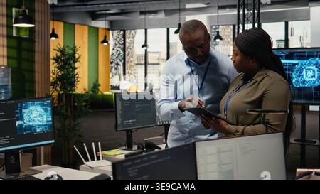 Engineers in startup office work with artificial intelligence driving market innovation. African american tech agency coworkers apply machine learning to optimize operations and efficiency, camera A Stock Photo