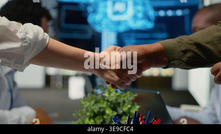 Programmer shaking hand with businessmen in tech agency boardroom. Angel investors meeting with AI startup company CTOs to hear technology presentation before investing, camera B Stock Photo