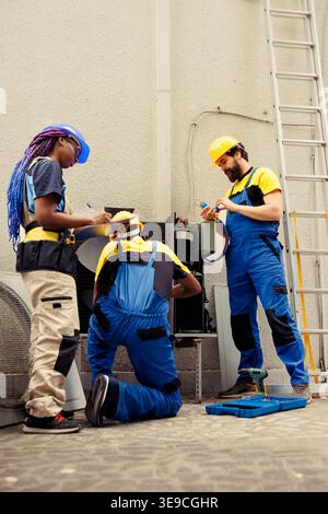 Diverse crew hired by home owner to service faulty air conditioner. Coworkers inspecting defective blower fan causing frozen evaporator coil, resulting in reduced cooling performance Stock Photo