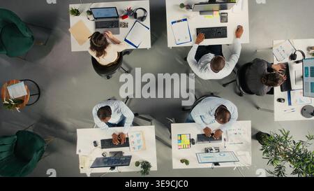 Top down view of business people gathered around laptops working on project tasks for development. Office environment promotes synergy, teamwork and insight through analytics. Stock Photo