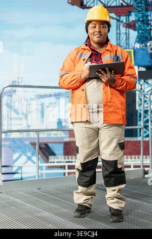 Portrait of smiling offshore platform employee using performance management program to reduce downtime. Happy woman uses laptop program integrating sensor readings to manage operations Stock Photo