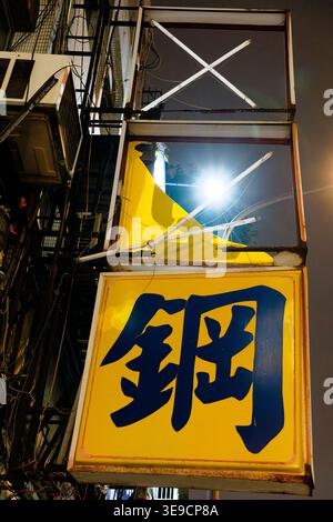 Taipei, Taiwan - December 25, 2024: Yellow "Gang" (steel) sign on a rusted frame with broken tubes and wiring on a worn Taipei street at night. Stock Photo