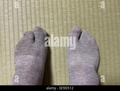 Traditional Japanese tabi split toe socks on two feet resting on a tatami mat Stock Photo