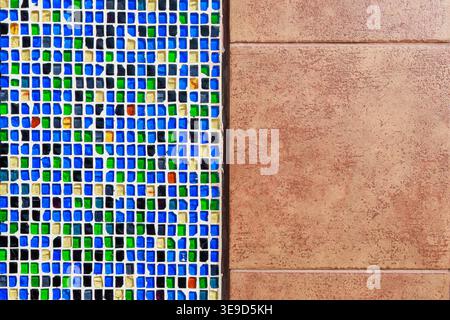 A vibrant close-up of a colorful mosaic tile wall featuring blue, green and yellow glass tiles with white grout, contrasted against a warm terracotta Stock Photo