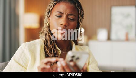 Confused, reading and phone with black woman on sofa in home for communication, mistake and scam. Contact, online glitch and phishing link with person Stock Photo