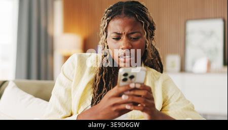 Confused, error and phone with black woman on sofa in home for communication, mistake and scam. Contact, online glitch and phishing link with person Stock Photo
