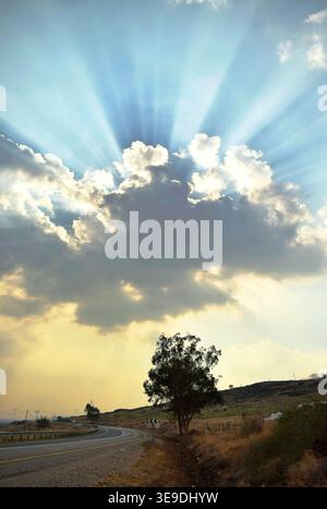 Dramatic dark thunderclouds, through which the sun rays scatter fan-shaped. An alarming end to the day Stock Photo
