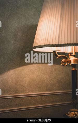 Old fashioned lamp with lampshade on a table. Hotel room design. Cozy home style. Classic home design. Bedroom lamp on table in the evening. Stock Photo