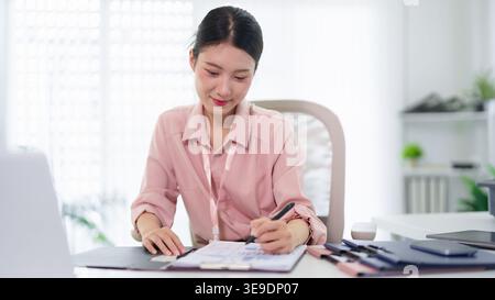 Young Asian businesswoman accountant calculating finance report with calculator and laptop at modern workspace desk Stock Photo