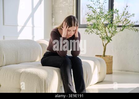 Unhappy upset stressed young woman sitting on sofa at home Stock Photo