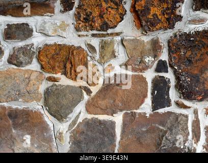 Multi colored stone and mortar surface with uneven thick mortar, cracked white mortar, and stones of various colors and sizes Stock Photo