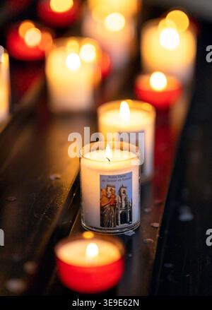A close-up shot of a glowing candle flame in a dark interior. One candle is in sharp focus while other burning candles create a beautiful soft bokeh e Stock Photo