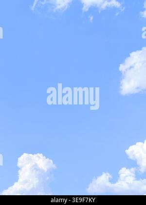 Vertical background texture of a bright clear blue sky with fluffy white cumulus clouds on a beautiful sunny summer day. Stock Photo