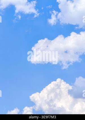 Vertical background texture of a bright clear blue sky with fluffy white cumulus clouds on a beautiful sunny summer day. Stock Photo