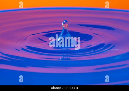 The bounce of a drop on a surface of colorful water with specular reflections Stock Photo