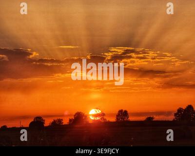 Sunset over rural landscape with dramatic orange sky and dark silhouettes in the foreground Stock Photo