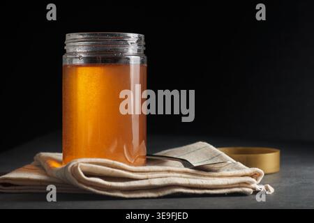 glass jar of golden honey on beige cloth napkin with metal spoon, dark textured background with copy space, natural sweetener breakfast concept Stock Photo