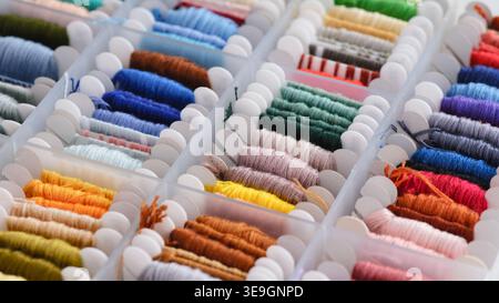 A close-up shot of a transparent plastic organizer box filled with various colorful embroidery threads neatly wound on white bobbins. Stock Photo