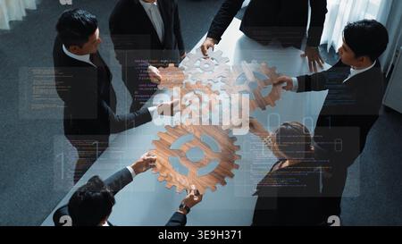 A diverse business team collaborates at a modern table, using wooden gear pieces to symbolize innovative thinking during a strategic planning session Stock Photo