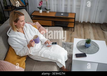 Woman relaxing at home with coffee mug holding remote control Stock Photo